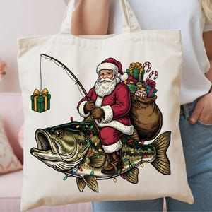 May include: A cream-colored canvas tote bag featuring a graphic illustration of Santa Claus riding a large fish. Santa wears a red suit, holds a fishing rod with a gift box on the line, and carries a brown sack filled with colorful wrapped presents.