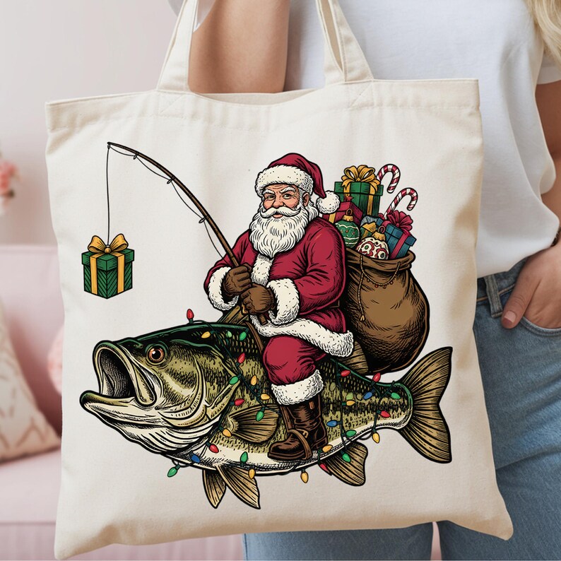May include: A cream-colored canvas tote bag featuring a graphic illustration of Santa Claus riding a large fish. Santa wears a red suit, holds a fishing rod with a gift box on the line, and carries a brown sack filled with colorful wrapped presents.