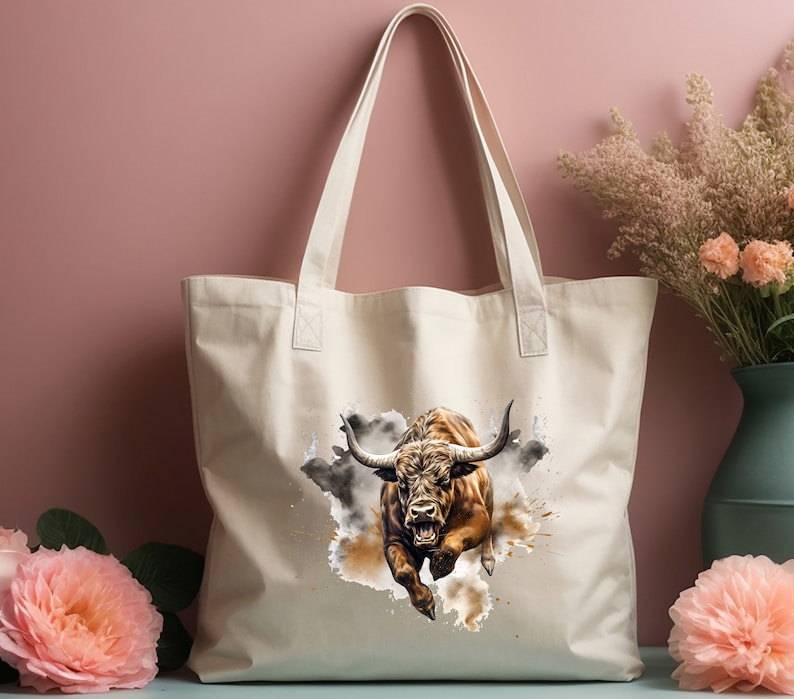 May include: A white canvas tote bag with a brown bull charging through a watercolor-style splash of brown and gray paint.