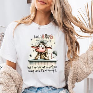 May include: White t-shirt featuring a cartoon donkey with the text "Not to BRAG" above the donkey and "but I can forget what I'm doing while I am doing it" below. The donkey is brown, with a pink nose and ears.