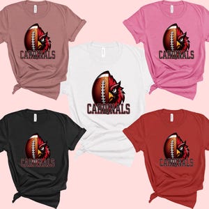 Puede incluir: Cinco camisetas de diferentes colores, cada una con un bal&oacute;n de f&uacute;tbol con un gr&aacute;fico de p&aacute;jaro cardenal y la palabra "CARDINALS" impresa en la parte delantera.