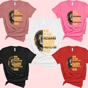 May include: Five t-shirts in different colors with a lion graphic and the text "Man of God, Husband, Daddy, Protector, Hero" in gold lettering.