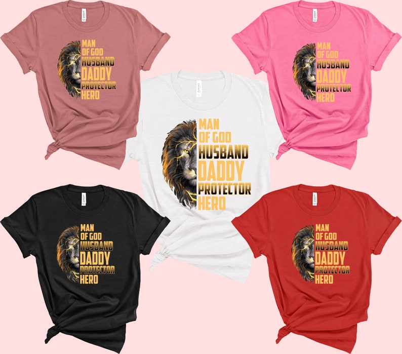 May include: Five t-shirts in different colors with a lion graphic and the text "Man of God, Husband, Daddy, Protector, Hero" in gold lettering.