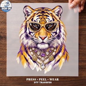 Peut inclure: Un transfert thermocollant DTF représentant un tigre portant des lunettes œil-de-chat à monture dorée et un collier doré à plusieurs rangs avec des pierres précieuses violettes et blanches. Texte : IRON ON, PRESS, PEEL, WEAR, DTF TRANSFER.