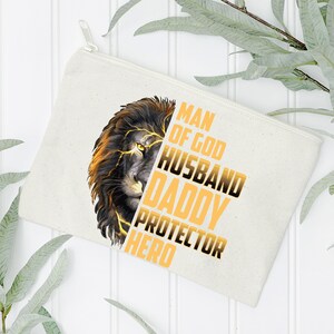 May include: A white canvas zippered pouch with a lion graphic and the text "Man of God Husband Daddy Protector Hero" in yellow.