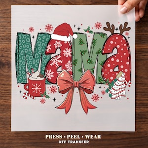 May include: A DTF transfer sheet featuring the word MAMA in large, stylized letters with varied Christmas patterns including leopard print, snowflakes, and trees. The design includes a Santa hat, a red bow, a cocoa mug, and reindeer antlers.