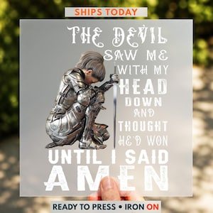 May include: A clear iron-on transfer sheet featuring a kneeling knight in silver armor holding a sword, with the text: THE DEVIL SAW ME WITH MY HEAD DOWN AND THOUGHT HE'D WON UNTIL I SAID AMEN. The design is printed in white and metallic silver tones.