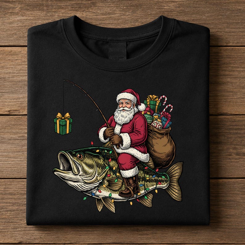 May include: A black t-shirt featuring a graphic of Santa Claus riding a large bass fish. Santa wears a red suit and holds a fishing rod with a gift box on the line. A sack of presents sits behind him, and the fish is decorated with colorful Christmas lights.