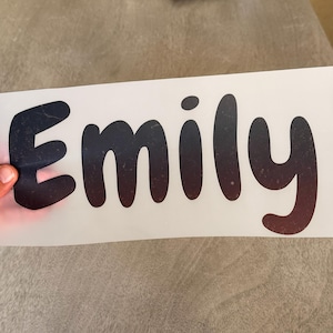 May include: A custom vinyl decal featuring the name Emily in a rounded, bold font. The lettering displays a dark gradient effect that transitions from black at the top to a deep reddish-brown at the bottom, set against a white backing sheet.