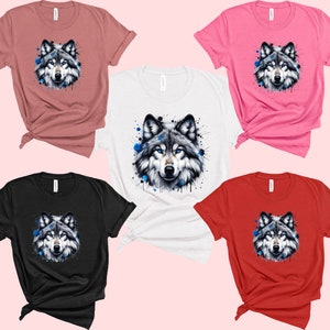 May include: Five t-shirts with different colors, each featuring a watercolor-style wolf with blue accents. The wolf is centered on each shirt.