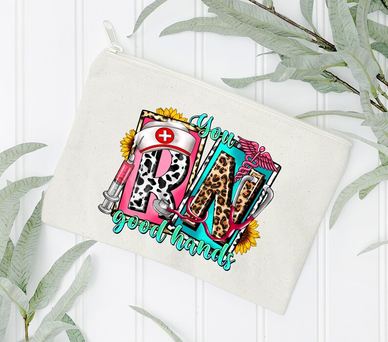 May include: A white canvas zippered pouch with a colorful graphic design featuring the letters "RN" in a leopard print and pink, with a stethoscope, a syringe, a sunflower, and the text "You good hands".