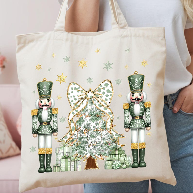 May include: A cream-colored canvas tote bag featuring a festive graphic print of two green nutcrackers standing on either side of a decorated Christmas tree with a large bow on top, surrounded by gold glitter snowflakes and gift boxes.