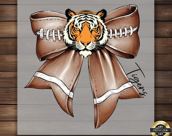 May include: A brown and white football-themed bow with a tiger head in the center. The bow has white stitching and the word "Tigers" is written on the right side.