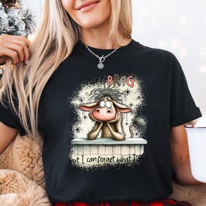 May include: Black t-shirt featuring a cartoon donkey with the text "Not to Brag but I can forget what I..." The donkey is resting its head on its hands. The shirt is a crew neck.