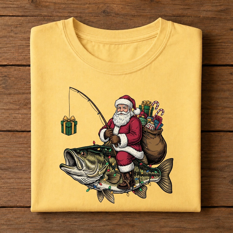 May include: A yellow t-shirt featuring a graphic of Santa Claus riding a large bass fish. Santa wears a red suit, carries a brown sack of gifts, and holds a fishing rod with a green gift box on the line. The fish is decorated with colorful lights.