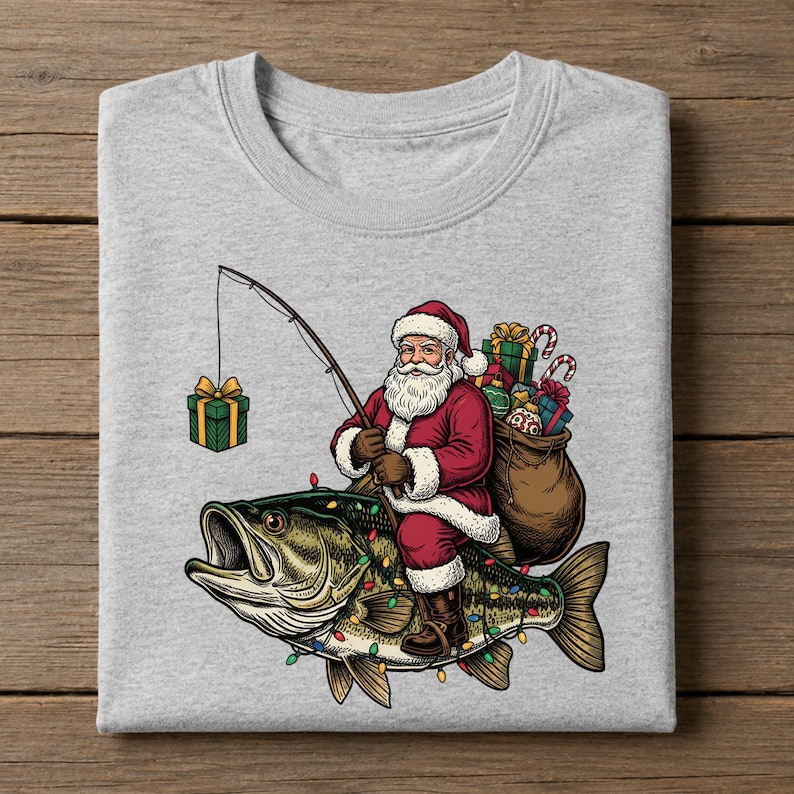 May include: A heather gray t-shirt featuring a graphic of Santa Claus riding a large bass fish. Santa holds a fishing rod with a gift box on the line. A sack of presents is on his back, and the fish is decorated with colorful Christmas lights.