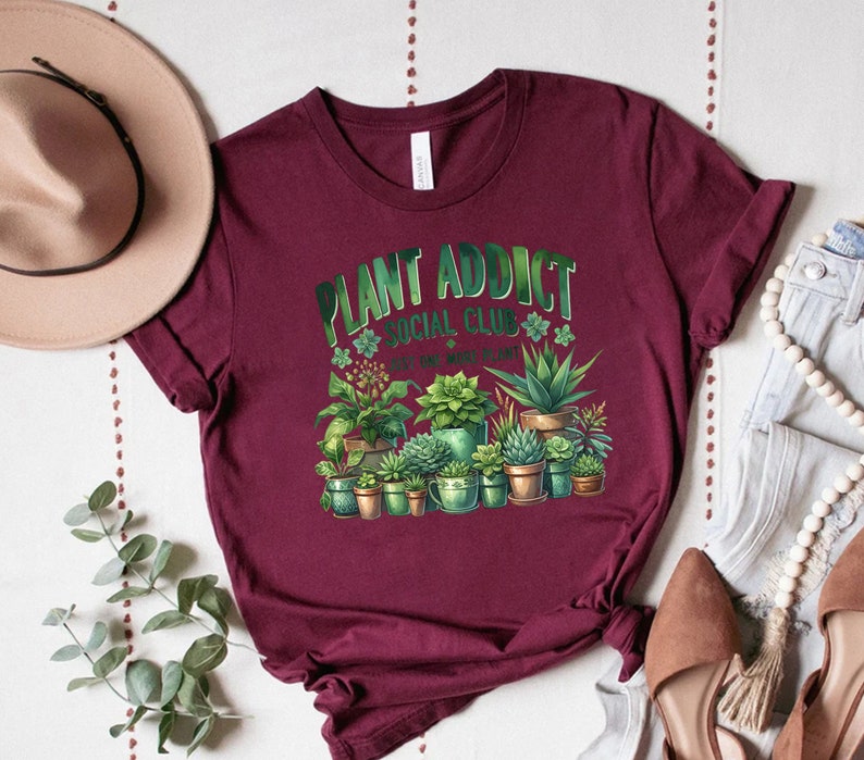 May include: Burgundy t-shirt with a green graphic of plants in pots and the text "Plant Addict Social Club - It's one more plant!"