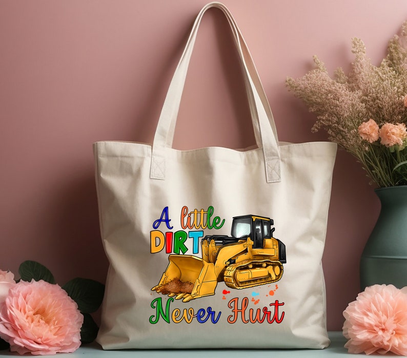 May include: A white canvas tote bag with a yellow bulldozer graphic and the text "A little dirt never hurt" in rainbow colors.