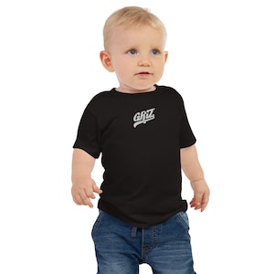 Puede incluir: Una camiseta negra de manga corta con un logotipo blanco "GRIZ" en la parte delantera. Un niño pequeño lleva la camiseta y mira hacia la derecha.
