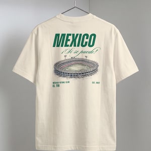 May include: Cream-colored t-shirt with a green graphic of a stadium and the word "MEXICO" above it. The text "¡Si se puede!" is above the stadium illustration. Below the stadium are the words "MÉXICO FUTBOL CLUB EL TRI" and "EST. 1927".