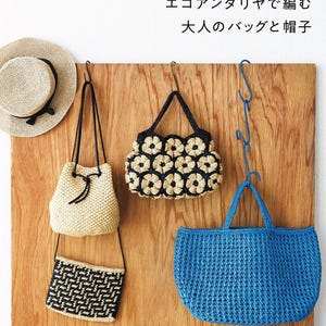 May include: A collection of crocheted items including a beige straw hat with a black ribbon, a beige drawstring pouch, a black and beige floral pattern handbag, a black and beige rectangular pouch, and a bright blue tote bag with text.
