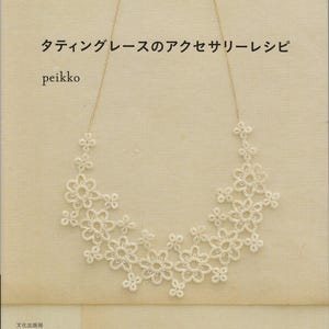Può includere: Primo piano di una collana di pizzo floreale bianco. La collana è esposta su un libro con testo giapponese. Il libro è intitolato "Tating Lace Accessory Recipe" di peikko.