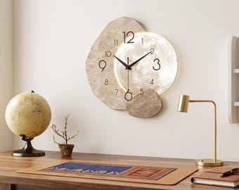 May include: A wall clock featuring a circular face with black numerals and hands, partially overlaid by an irregular, textured beige stone-like frame. The clock design incorporates a smooth, metallic-toned circular section behind the hands.