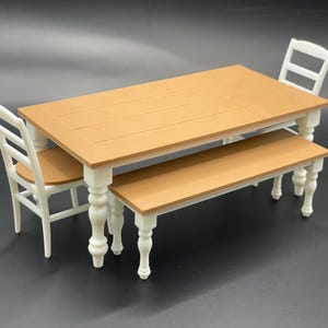 May include: A white farmhouse style dining set with a wooden table, two chairs, and a bench. The table has a brown top and white legs. The chairs and bench have white frames and brown seats.