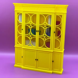 以下が含まれることがあります： ガラス扉と装飾的な円形デザインが特徴の明るい黄色のキャビネット。キャビネットには複数の棚と収納コンパートメントがあり、バインダーやボックスなど、さまざまなアイテムが収納されています。キャビネットは紫色の背景に配置されています。