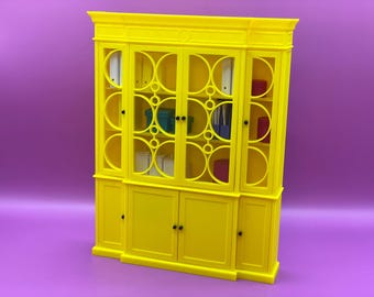 Può includere: Un mobile giallo brillante con ante in vetro e un design circolare decorativo. Il mobile ha più ripiani e vani portaoggetti, con vari oggetti all'interno, tra cui raccoglitori e scatole. Il mobile è posto su uno sfondo viola.