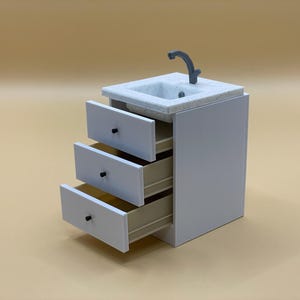 May include: White vanity unit with a marble worktop and a small sink with a tap. The unit has three drawers, one of which is open.