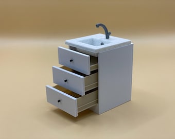May include: White vanity cabinet with a marble countertop and a small sink with a faucet. The cabinet has three drawers, one of which is open.