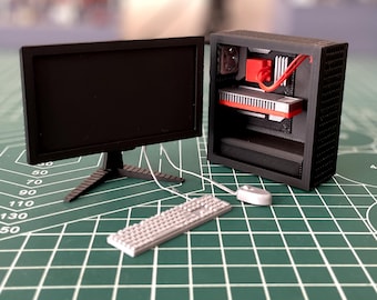 May include: A miniature black computer with a black monitor, a white keyboard, and a white mouse. The computer is on a green cutting mat.