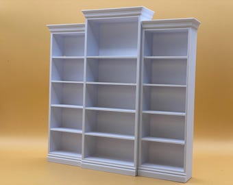 Può includere: Tre librerie bianche con più ripiani. Le librerie sono di larghezze e altezze variabili, con un design classico con modanature sulla parte superiore e una modanatura sulla base. I ripiani sono vuoti.