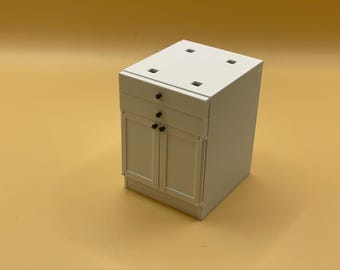 May include: White kitchen cabinet with two doors and a drawer. The cabinet has black knobs and is made of wood.