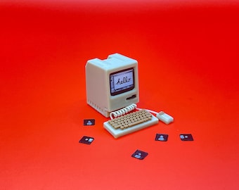Puede incluir: Un ordenador de sobremesa de estilo vintage con una carcasa blanca y una pantalla que muestra la palabra "hello". El ordenador está acompañado de un teclado y un ratón, y hay varios disquetes esparcidos a su alrededor.