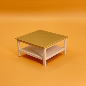 May include: A white two-tiered coffee table with a gold top. The table has a square shape and is made of wood.