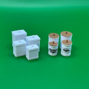 May include: Set of six white ceramic canisters with lids. Four canisters are square and two are round. The round canisters have brown lids and are labelled "Sugar" and "Powdered Sugar".