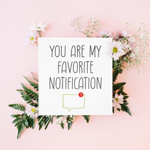 May include: A white card with the text "You are my favourite notification" and a green speech bubble with a red notification dot. The card is surrounded by white and pink flowers on a pink background.