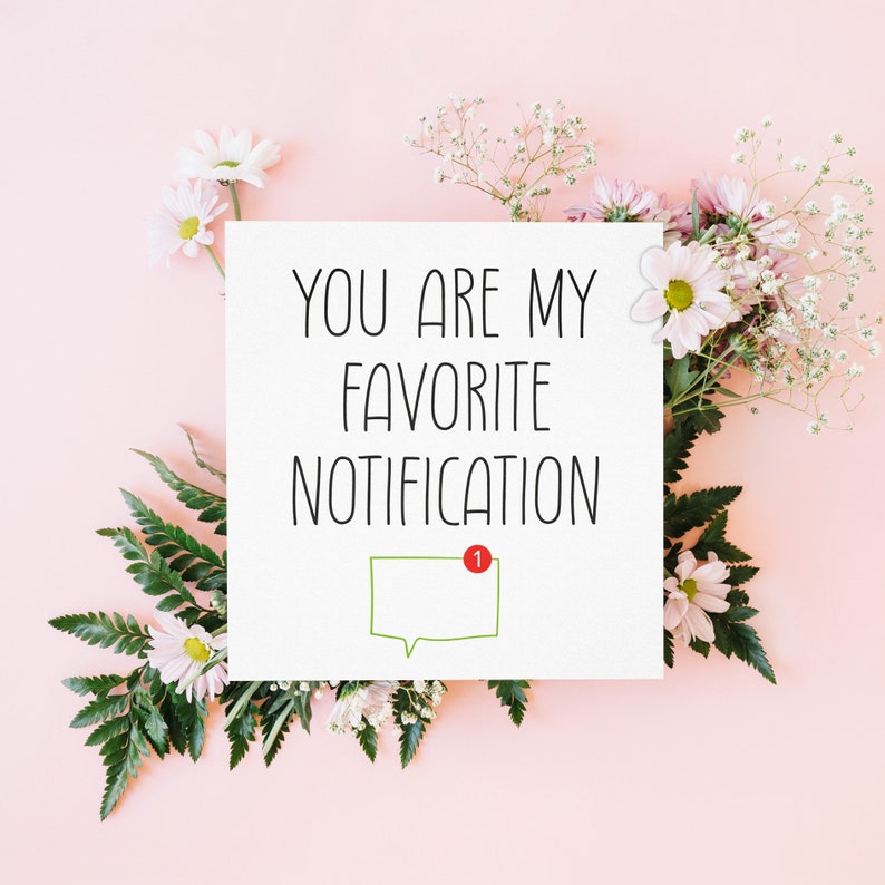 May include: A white card with the text "You are my favourite notification" and a green speech bubble with a red notification dot. The card is surrounded by white and pink flowers on a pink background.