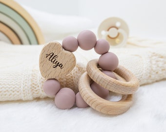 May include: A pink and wooden baby teether with a heart-shaped wooden tag that says "Aliya".
