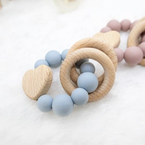 May include: A wooden teething ring with a heart-shaped piece and blue silicone beads.
