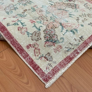 Puede incluir: Una alfombra vintage con fondo crema y borde rojo. La alfombra tiene un patrón floral con acentos rosa, verde y marrón. La alfombra está flecos en todos los lados.