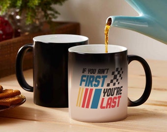 May include: Black magic mug with the text "If you ain't first you're last" in colourful letters and a chequered flag graphic. The mug is filled with coffee.