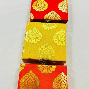 May include: A stack of four rectangular boxes with ornate gold leaf patterns on a variety of colored backgrounds. The colors include pink, red, yellow, and orange. The boxes are likely for jewelry or small gifts.
