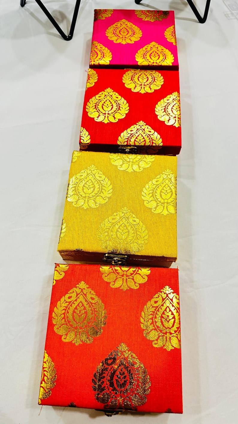 May include: A stack of four rectangular boxes with ornate gold leaf patterns on a variety of colored backgrounds. The colors include pink, red, yellow, and orange. The boxes are likely for jewelry or small gifts.