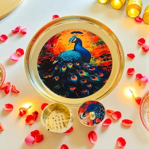 May include: A decorative serving tray with a gold rim and a vibrant peacock design. The peacock is depicted with blue, green, and yellow feathers against a colorful floral background. A small matching container and lid are also present.
