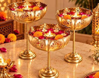 Puede incluir: Tres cuencos de metal dorado sobre pedestal con bordes festoneados y patrones de loto recortados. Cada cuenco contiene agua, pétalos de flores rosas y blancas, caléndulas naranjas y una pequeña vela de té encendida en el centro.