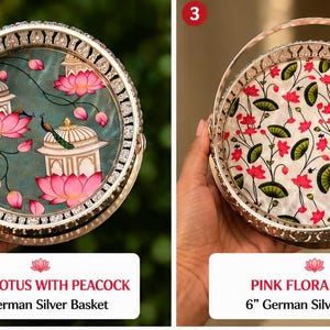 May include: Two round 6-inch German silver baskets with handles. The left basket features a green background with pink lotus flowers, white structures, and a peacock. The right basket has a white background with a pink and green floral pattern.