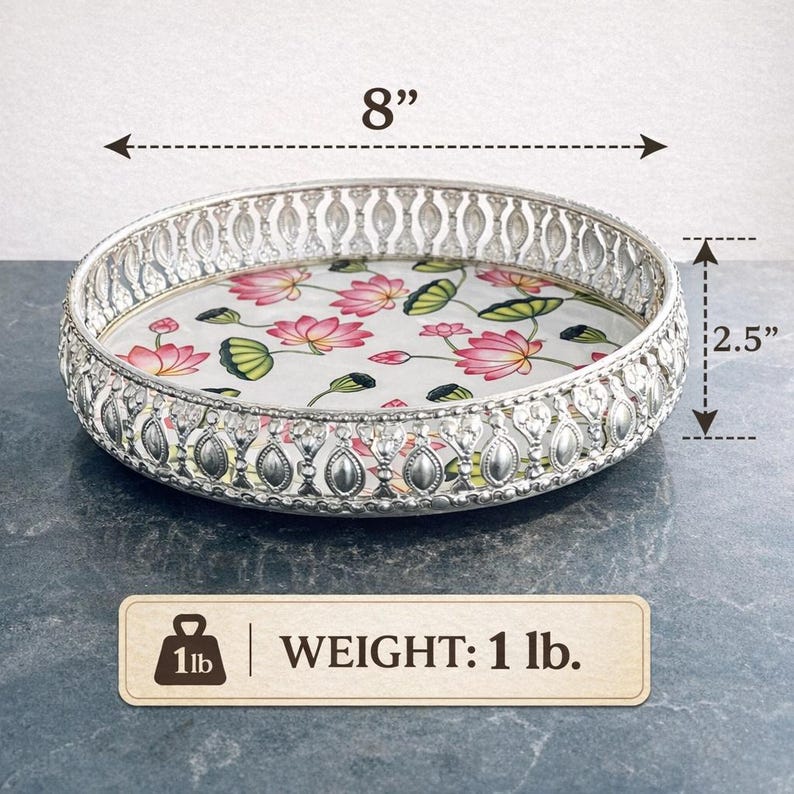 May include: A round silver-toned metal tray with an intricate openwork rim and a floral base featuring pink lotus flowers and green leaves. The tray measures 8 inches in diameter and 2.5 inches in height, with a total weight of 1 lb.